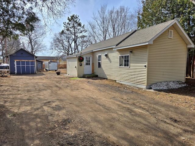 exterior space featuring entry steps, a detached garage, a storage shed, an outdoor structure, and a shingled roof