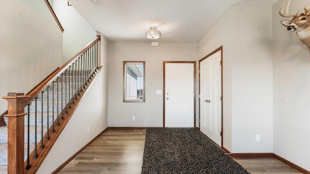 foyer entrance with stairway, baseboards, and wood finished floors