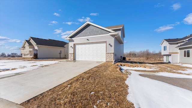 view of snowy exterior with a garage, stone siding, and concrete driveway