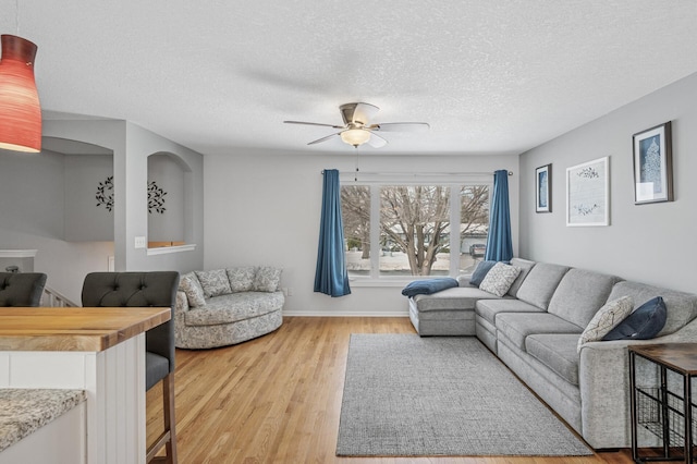 living area with a textured ceiling, light wood-style floors, baseboards, and ceiling fan