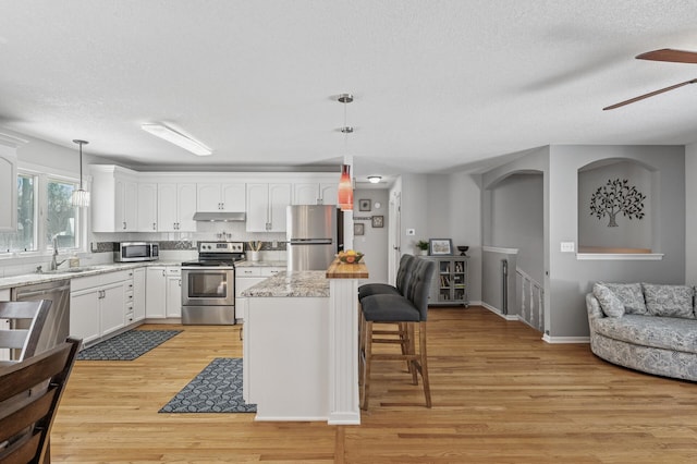 kitchen with light wood finished floors, white cabinets, appliances with stainless steel finishes, under cabinet range hood, and a kitchen breakfast bar