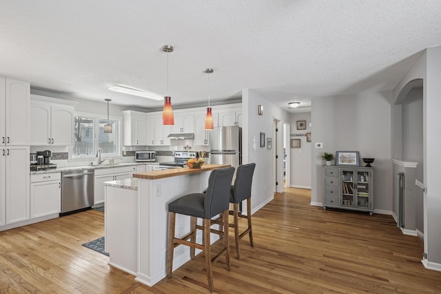 kitchen featuring a breakfast bar, under cabinet range hood, white cabinetry, light wood-style floors, and appliances with stainless steel finishes