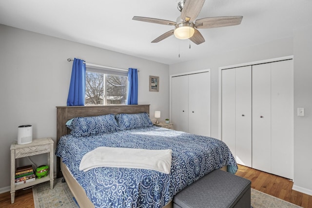 bedroom with a ceiling fan, wood finished floors, baseboards, and two closets