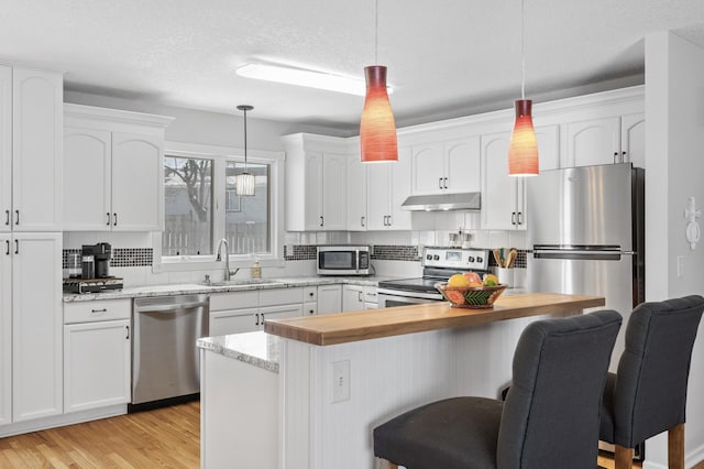 kitchen featuring a breakfast bar, under cabinet range hood, wood counters, a sink, and appliances with stainless steel finishes