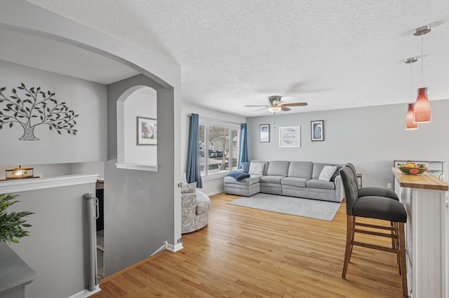 living area with ceiling fan, baseboards, a textured ceiling, and light wood-style flooring