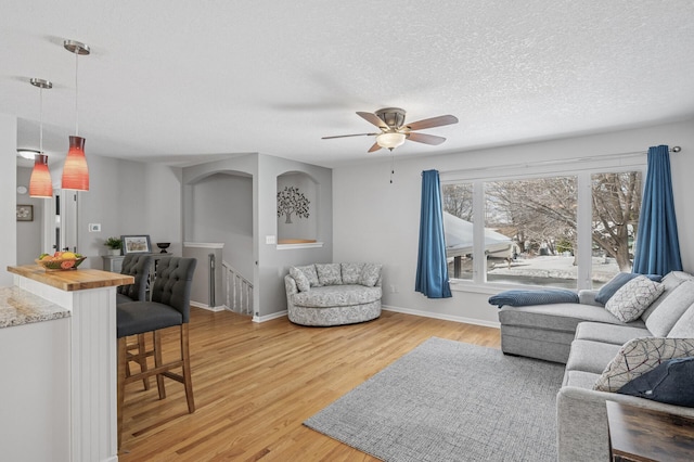 living area with baseboards, light wood-style floors, a ceiling fan, and a textured ceiling