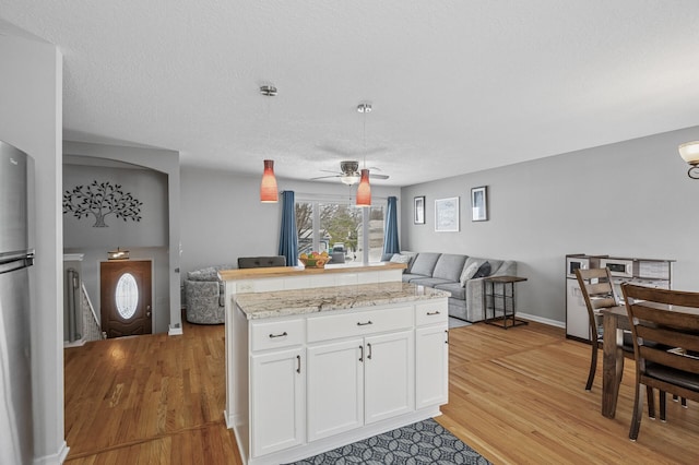 kitchen featuring ceiling fan, open floor plan, light wood-type flooring, hanging light fixtures, and white cabinetry