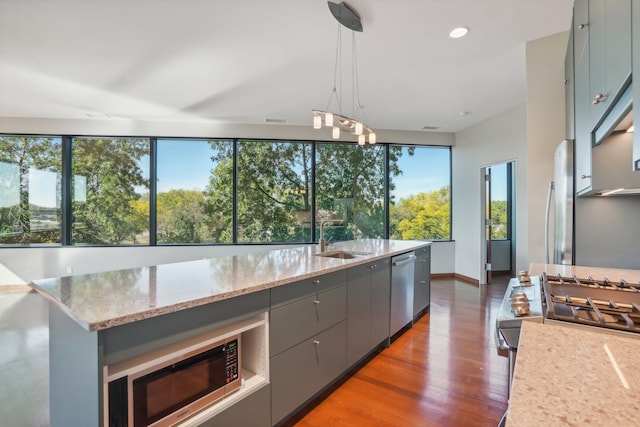 kitchen featuring light stone countertops, wood finished floors, gray cabinets, a sink, and appliances with stainless steel finishes