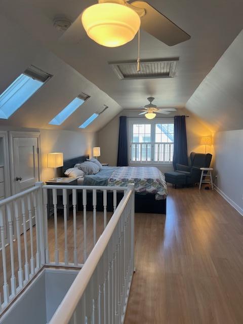 bedroom with baseboards, vaulted ceiling with skylight, wood finished floors, and a ceiling fan