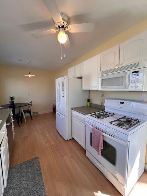 kitchen with dark countertops, pendant lighting, light wood-type flooring, white cabinets, and white appliances