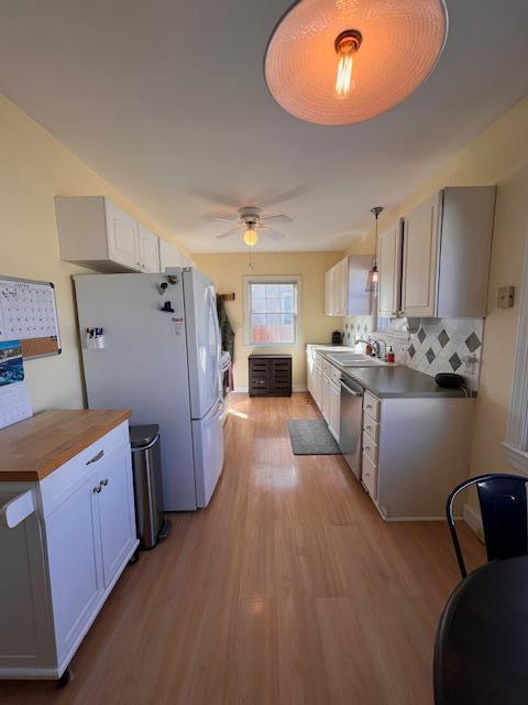 kitchen with tasteful backsplash, light wood-type flooring, stainless steel dishwasher, freestanding refrigerator, and a sink