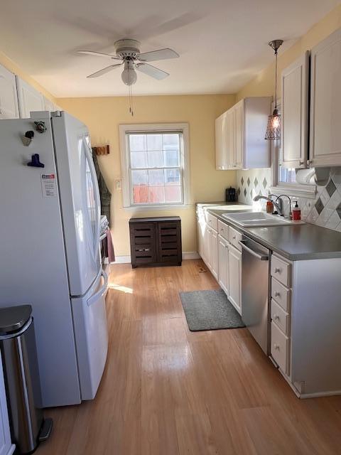 kitchen featuring dishwasher, decorative backsplash, light wood-style flooring, freestanding refrigerator, and a sink