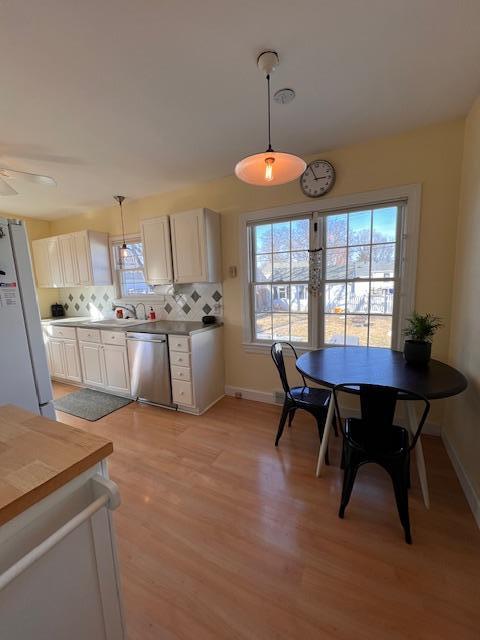 kitchen featuring backsplash, dishwasher, pendant lighting, freestanding refrigerator, and plenty of natural light