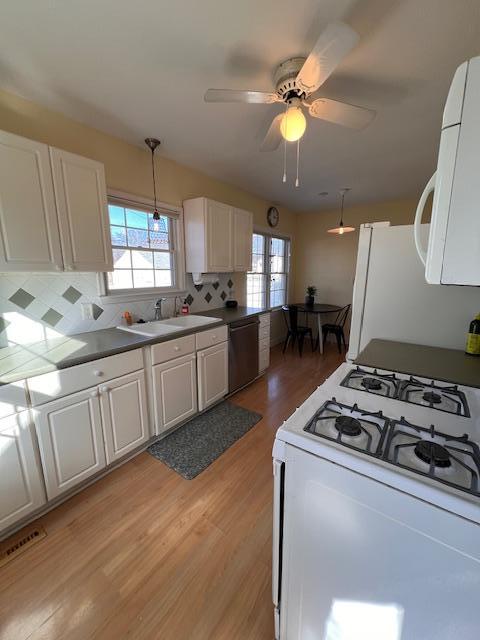 kitchen with a sink, white appliances, light wood-style floors, white cabinets, and a healthy amount of sunlight