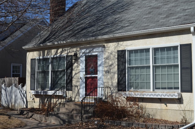 doorway to property featuring stucco siding, a shingled roof, a chimney, and fence