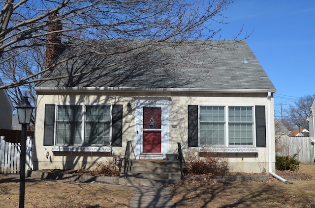 cape cod home featuring stucco siding, entry steps, a shingled roof, and fence