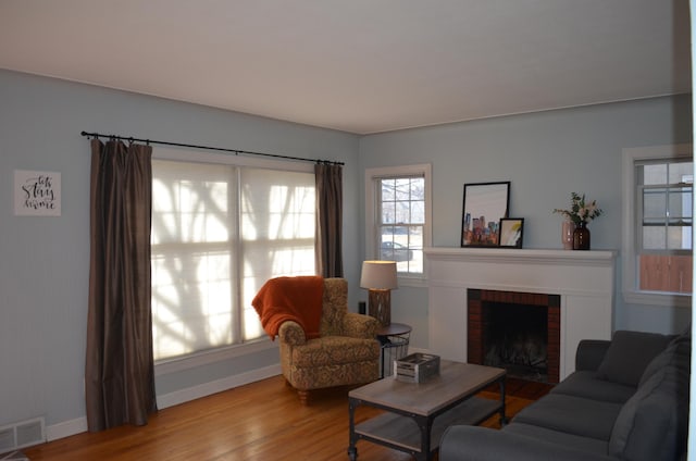 living area featuring a fireplace, wood finished floors, visible vents, and baseboards