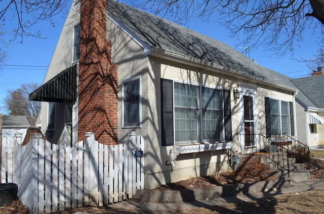 view of side of home featuring roof with shingles, a chimney, and fence