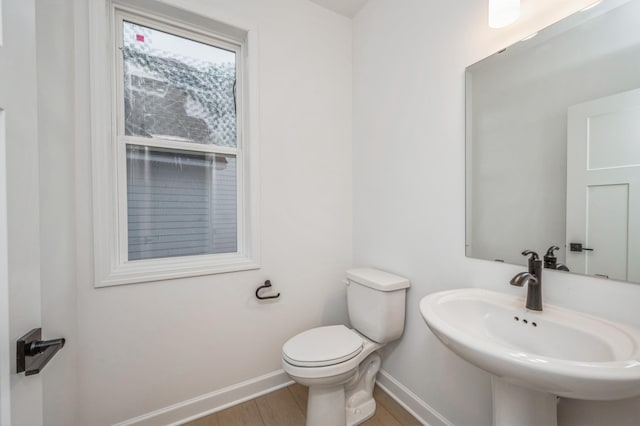 half bath with wood finished floors, toilet, baseboards, and a sink