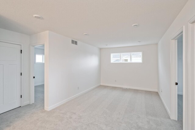 spare room with light colored carpet, visible vents, a wealth of natural light, and baseboards