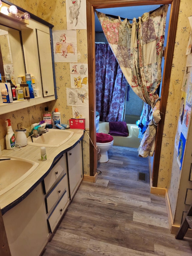 bathroom with visible vents, toilet, wood finished floors, wallpapered walls, and double vanity