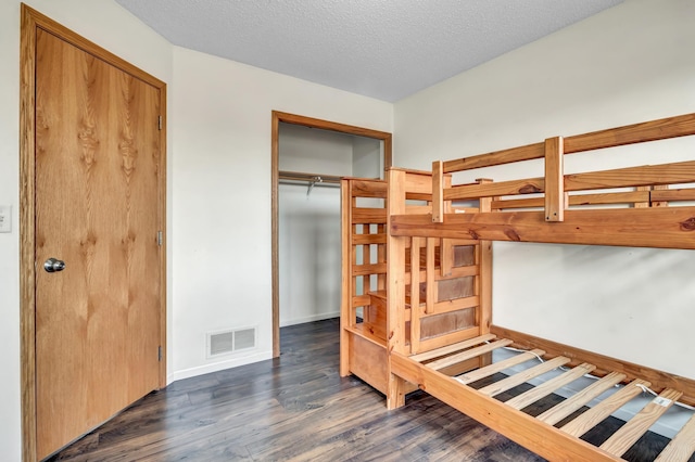 bedroom featuring dark wood-style floors, baseboards, visible vents, a closet, and a textured ceiling