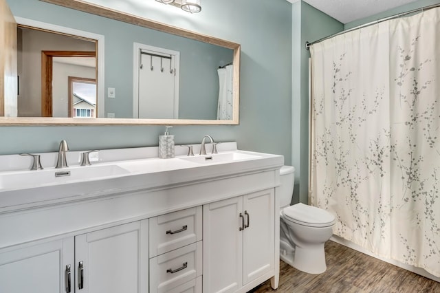 full bath with toilet, a shower with shower curtain, double vanity, wood finished floors, and a sink