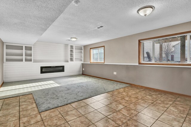 unfurnished living room featuring built in features, a textured ceiling, baseboards, and a glass covered fireplace