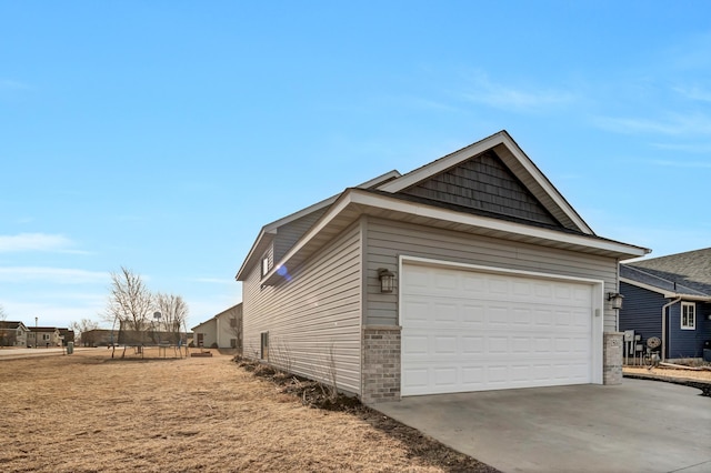 view of side of home with brick siding, driveway, an attached garage, and a trampoline