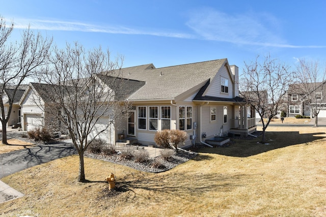 view of front of property with driveway, an attached garage, a chimney, a shingled roof, and a front lawn