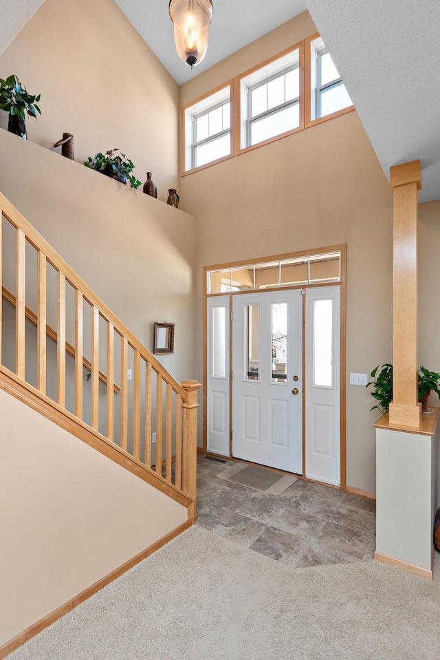 foyer featuring baseboards, a high ceiling, carpet flooring, and ornate columns