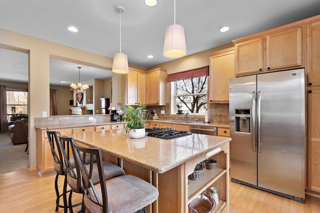 kitchen featuring light wood-type flooring, light stone counters, tasteful backsplash, a kitchen island, and appliances with stainless steel finishes