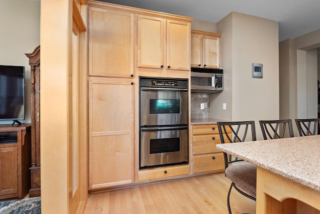 kitchen with light brown cabinetry, light stone counters, light wood-style floors, appliances with stainless steel finishes, and decorative backsplash