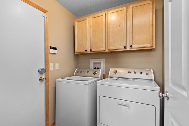 washroom featuring cabinet space, a textured ceiling, and washing machine and clothes dryer