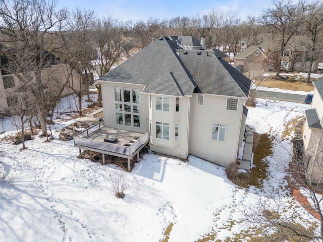 snow covered rear of property with a deck and a shingled roof