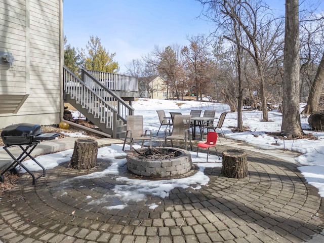 snow covered patio featuring a grill, a deck, stairs, and an outdoor fire pit