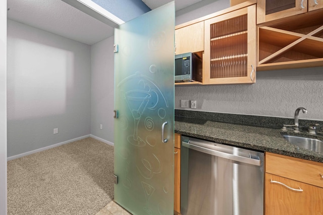 kitchen featuring a sink, stainless steel appliances, dark stone counters, baseboards, and light colored carpet