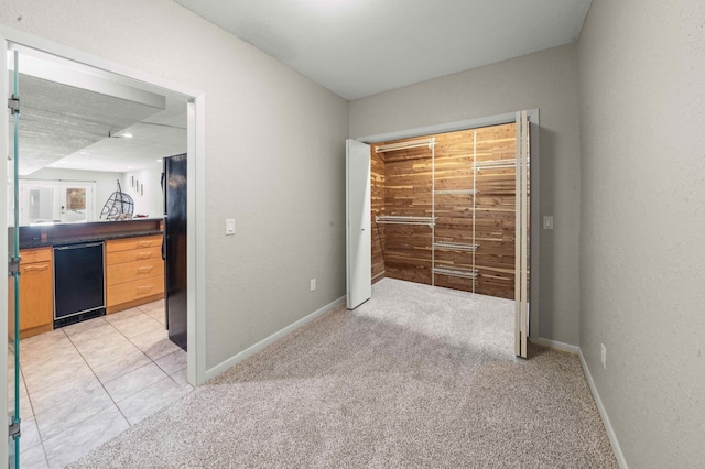 unfurnished bedroom with a textured wall, baseboards, freestanding refrigerator, and light carpet