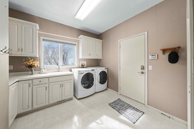 laundry area with baseboards, light floors, cabinet space, independent washer and dryer, and a sink