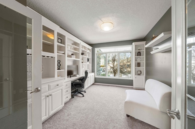 office area featuring light colored carpet, built in desk, and a textured ceiling