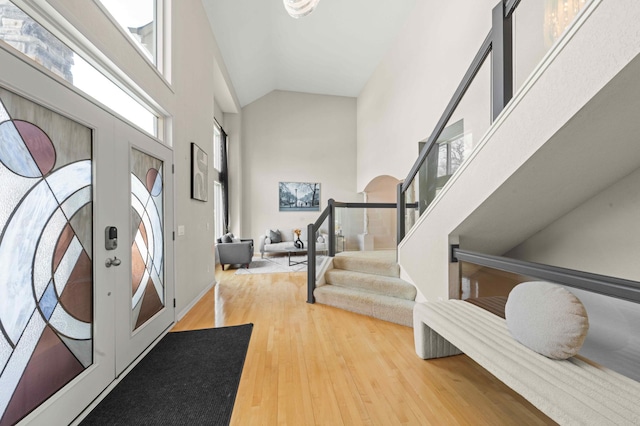 foyer entrance with stairway, wood finished floors, and high vaulted ceiling