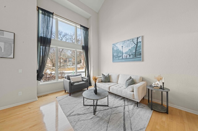 living area featuring a wealth of natural light, baseboards, high vaulted ceiling, and wood finished floors