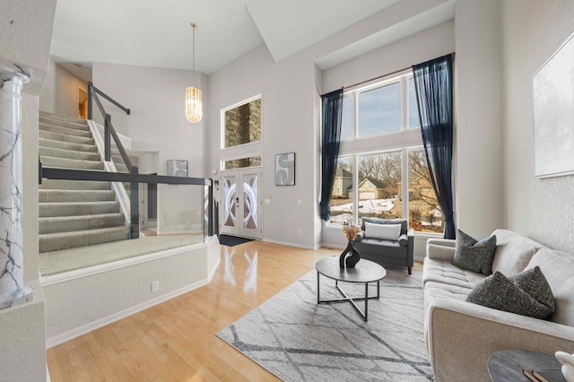 living room featuring a notable chandelier, wood finished floors, a high ceiling, baseboards, and stairs