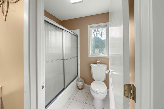 bathroom with tile patterned flooring, toilet, baseboards, and enclosed tub / shower combo