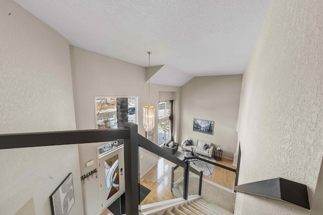 stairway with a chandelier, a textured wall, vaulted ceiling, wood finished floors, and a textured ceiling