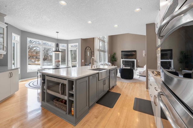 kitchen with a fireplace, gray cabinetry, light countertops, stainless steel microwave, and light wood-type flooring