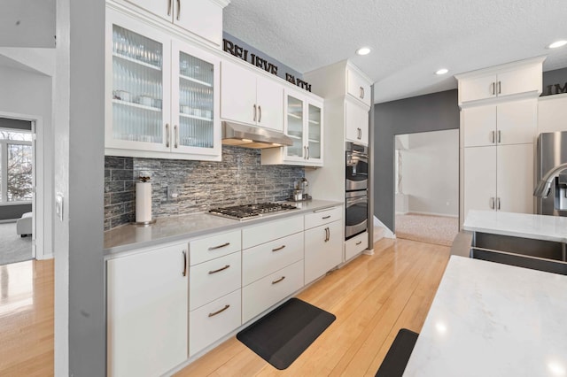 kitchen featuring tasteful backsplash, under cabinet range hood, light countertops, white cabinets, and stainless steel appliances