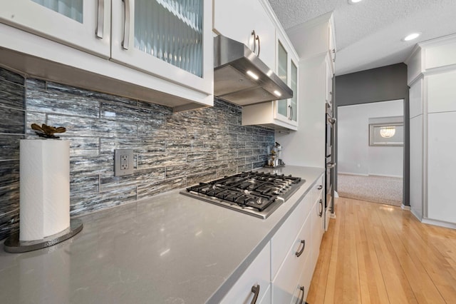 kitchen featuring a textured ceiling, ventilation hood, appliances with stainless steel finishes, white cabinets, and light wood finished floors