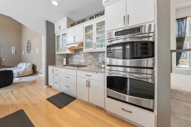 kitchen with light wood finished floors, backsplash, under cabinet range hood, light countertops, and appliances with stainless steel finishes