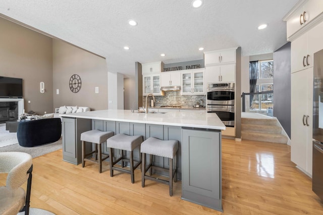 kitchen featuring stainless steel double oven, backsplash, a breakfast bar area, and white cabinetry